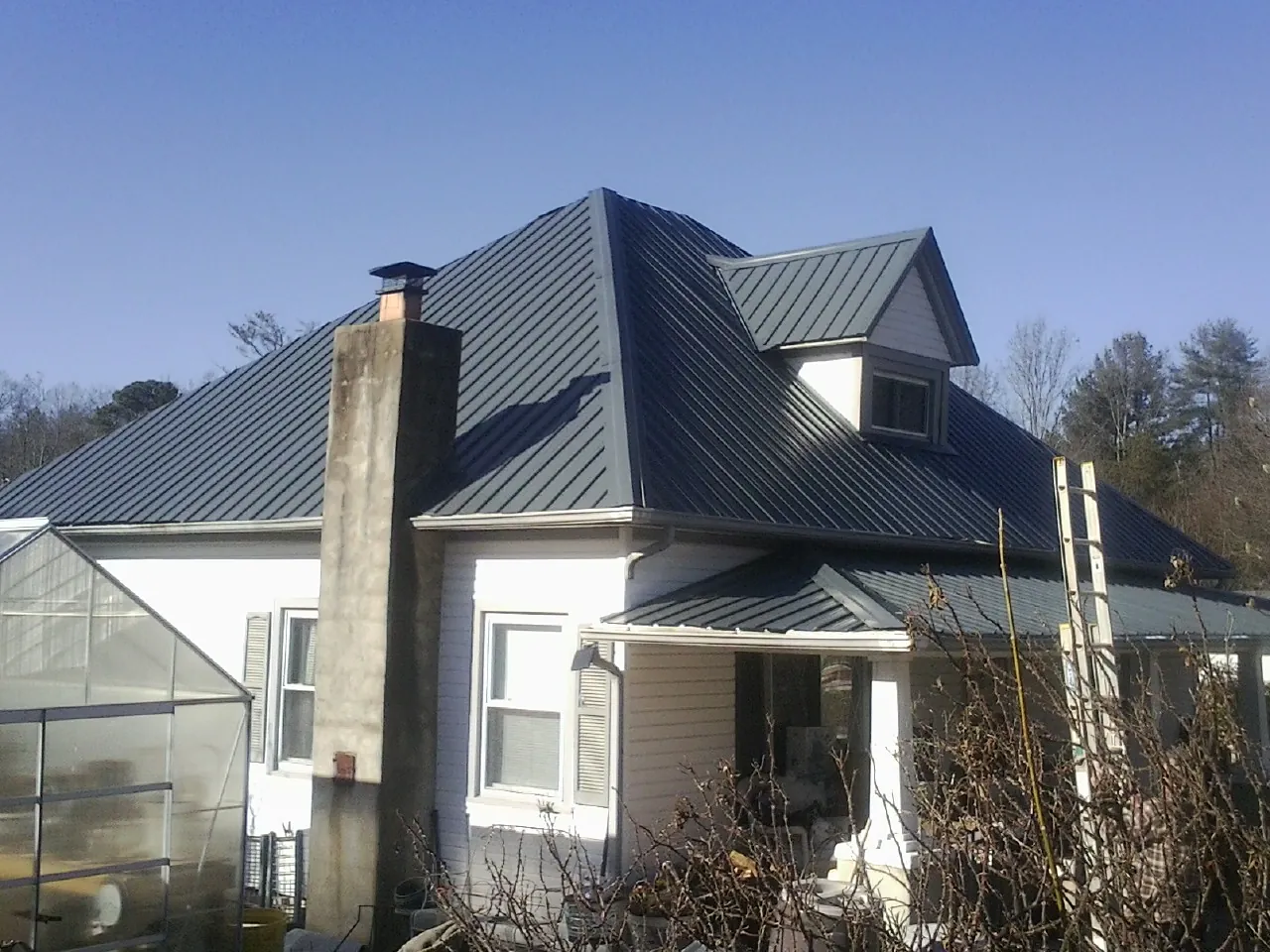 Dark blue standing seam metal roof on a white farmhouse with dormer — Slate & Tile Roof Repair by Roofing Brothers in Booneville