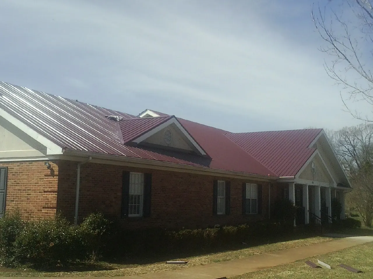 Red metal roof with gabled entries on a long brick building, from a Hail Damage Roof Repair job in Booneville