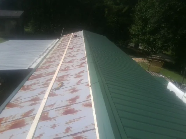 Old rusted panels beside newly installed green metal roofing — Wind Damage Roof Repair by Roofing Brothers in Booneville