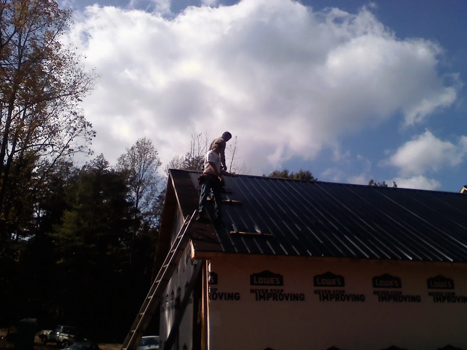 Roofer fastening dark metal panels high against a cloudy sky, from a Roof Inspection job in Booneville