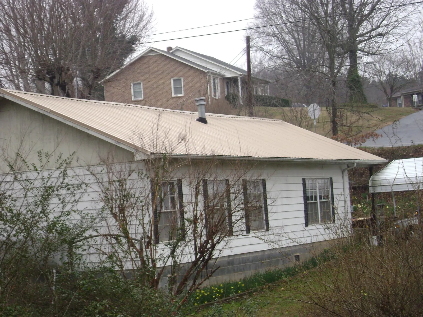 Tan metal roof on a white sided house set into a hillside — Commercial Roofing by Roofing Brothers in Booneville
