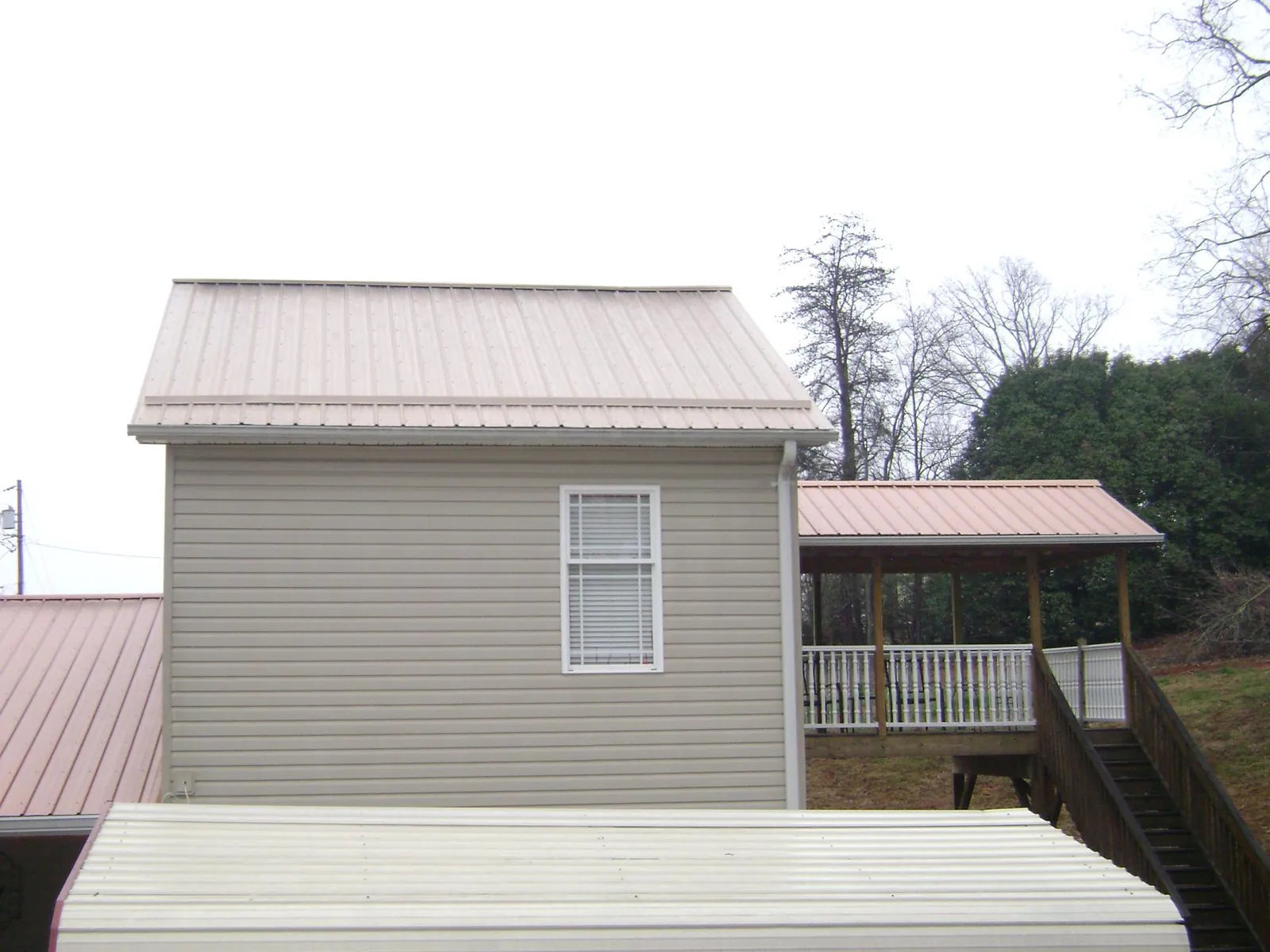 Tan metal roofs on a two story addition and attached porch, from a Roof Replacement job in Booneville