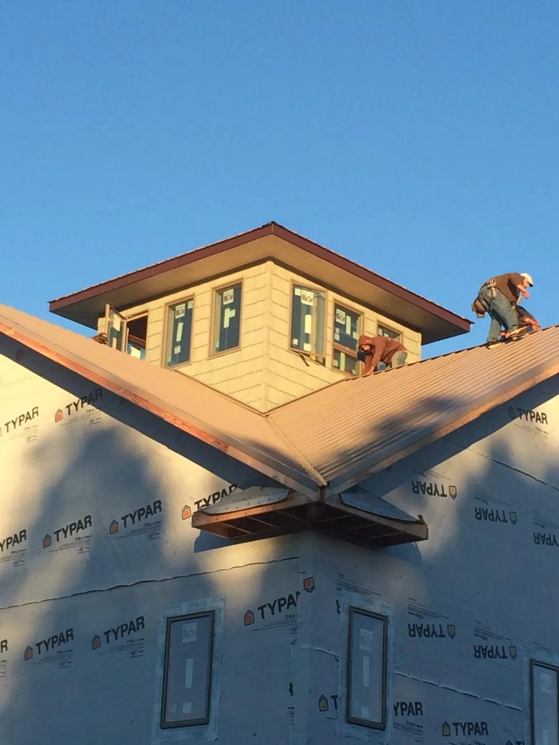 Roofers working around a rooftop cupola on a new metal roof at sunset — Roof Waterproofing in Booneville by Roofing Brothers